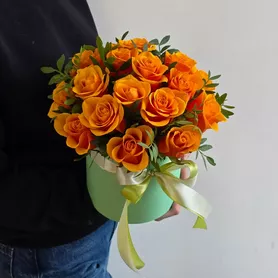 Яркие оранжевые розы Испания в шляпной коробке с зеленью фисташки от интернет-магазина «Чёткий букет» в Воронеже